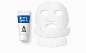 تیوب ژل کربوکسی ریباسکین در کنار ماسک ورقهای صورت و گردن روی پسزمینه سفید؛ ترکیب محصول برای کربوکسیتراپی خانگی